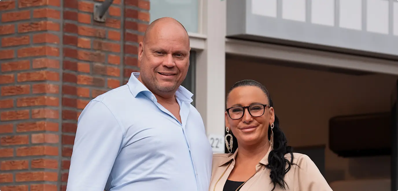 a man and woman stand together outside a building, engaged in conversation under a clear sky